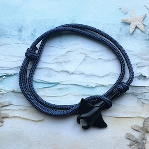 Puede incluir: Un brazalete de cordón azul marino con un dije de manta raya negra.