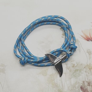 Puede incluir: Un brazalete de cuerda azul y dorado con un dije de cola de ballena plateado.