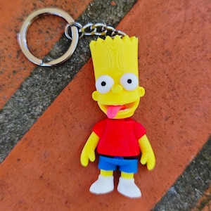 May include: A Bart Simpson keychain featuring the character in his signature outfit. The keychain has a yellow head, red shirt, blue shorts, and white shoes. The keychain is attached to a silver metal ring and chain.