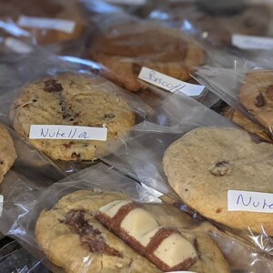 May include: A variety of cookies in clear plastic bags, labeled with their flavors: Nutella, Bueno, and Biscoff. The cookies are arranged in a row, with the labels facing the viewer.