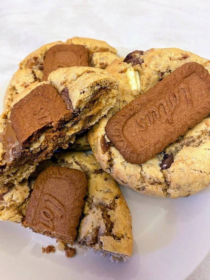 May include: Close-up of four chocolate chip cookies with a caramel filling and a chocolate and caramel biscuit on top. The cookies are on a white plate.