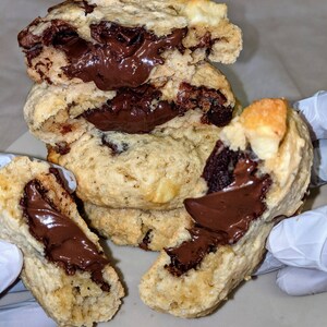 May include: A stack of chocolate chip cookies with a thick layer of chocolate spread inside. The cookies are light brown and have a slightly crispy texture.