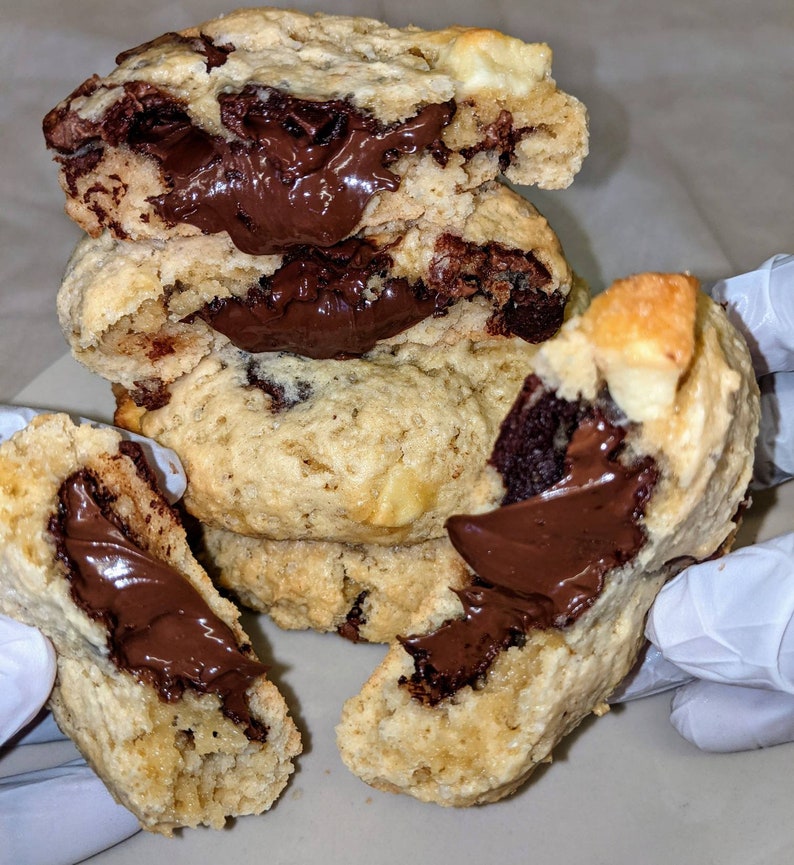 May include: A stack of chocolate chip cookies with a thick layer of chocolate spread inside. The cookies are light brown and have a slightly crispy texture.