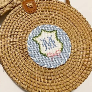 May include: Three straw bags with embroidered circles featuring the initials "KK" in blue and pink thread. The bags are woven with a natural brown color.