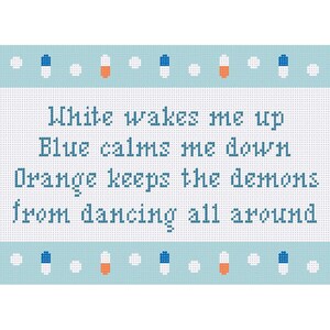 May include: A cross-stitch design on a light blue background. The text reads "White wakes me up, Blue calms me down, Orange keeps the demons from dancing all around." The design includes orange, white, and blue pill-shaped accents.