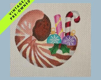 May include: A hand-stitched Christmas ornament featuring a peppermint candy design with brown and white stripes. Inside the candy is a collection of ornaments, candy canes, and holly. The words "VINTAGE / PRE-OWNED" are on a diagonal green banner.