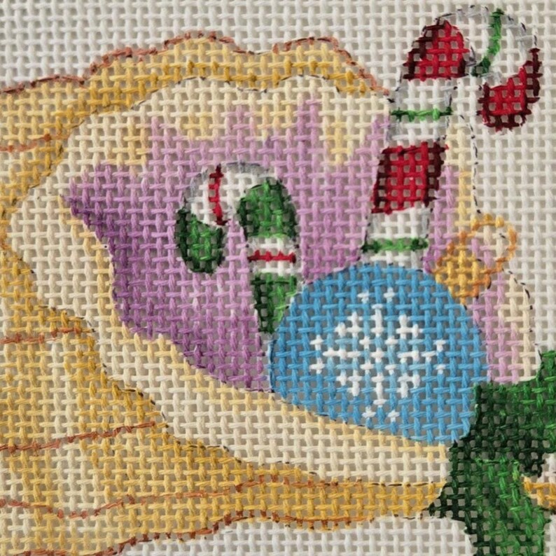 May include: Needlepoint design featuring a Christmas ornament, candy canes, and a floral element. The ornament is blue with a white snowflake design. Candy canes are red and white. The floral element has yellow, purple, and green hues.