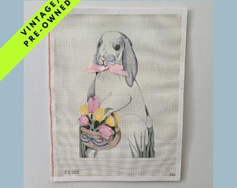 May include: Vintage pre-owned needlepoint art featuring a gray bunny with a pink bow tie, holding a basket of yellow and pink tulips. The artwork is on a checkered background with a green and yellow banner that says "VINTAGE / PRE-OWNED".