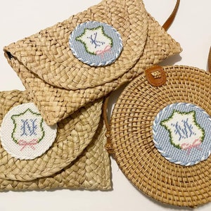 May include: Three straw bags with embroidered initials in a blue and white circle. The bags are woven and have a natural brown color.