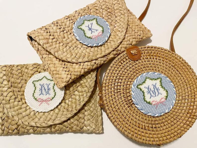 May include: Three straw bags with embroidered initials in a blue and white circle. The bags are woven and have a natural brown color.