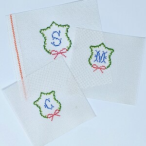 May include: Three white canvas panels with green, blue, and red embroidered designs. Each panel features a shield-shaped design with a letter inside. The letters are "S", "M", and "C".
