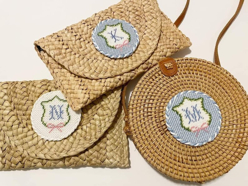 May include: Three straw bags with embroidered circles featuring the initials "KK" in blue and pink thread. The bags are woven with a natural brown color.