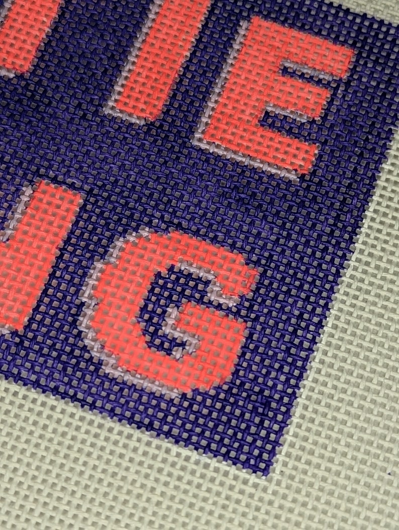 May include: Close-up of a red and white embroidered word "LIVE" on a blue and white canvas background.
