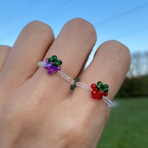 Peut inclure: Deux bagues en perles avec des bandes transparentes et des motifs de fruits. Une bague a un motif de raisin violet avec des feuilles vertes. L'autre bague a un motif de fraise rouge avec des feuilles vertes.