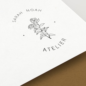 Puede incluir: Logotipo en blanco y negro con el texto "SARAH NOAH ATELIER" en un c&iacute;rculo alrededor de un dise&ntilde;o floral estilizado.