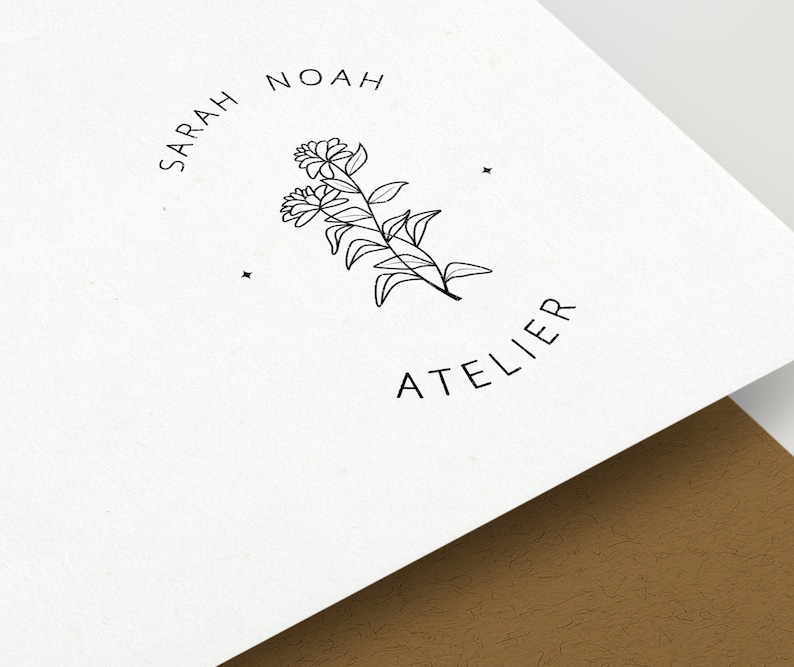 Puede incluir: Logotipo en blanco y negro con el texto "SARAH NOAH ATELIER" en un c&iacute;rculo alrededor de un dise&ntilde;o floral estilizado.
