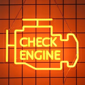 Pode incluir: Uma placa de néon amarela brilhante em forma de motor de carro, com as palavras "CHECK ENGINE". A placa está pendurada em um fundo laranja com um padrão de grade preta. A placa iluminada é provavelmente feita de vidro e é suspensa por correntes.
