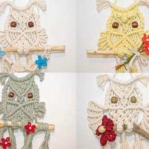 May include: Four macrame owl wall hangings in cream, yellow, grey, and off-white. Each owl has wooden bead eyes and sits on a wooden perch. Some owls have floral accents in red and blue.