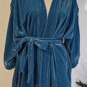 May include: A teal blue velvet robe with a long, flowing design. The robe has a V-neck and a tie belt.