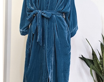 May include: A teal blue velvet robe with a long, flowing silhouette. The robe has a V-neckline, long sleeves, and a tie belt. It is made of a soft, luxurious fabric.