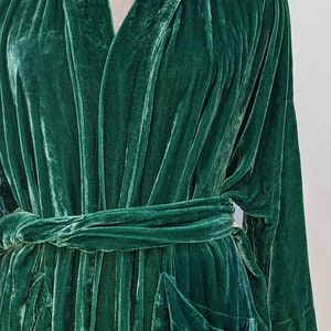 May include: A dark green velvet robe with a shawl collar and a tie belt. The robe has two large pockets on the front.