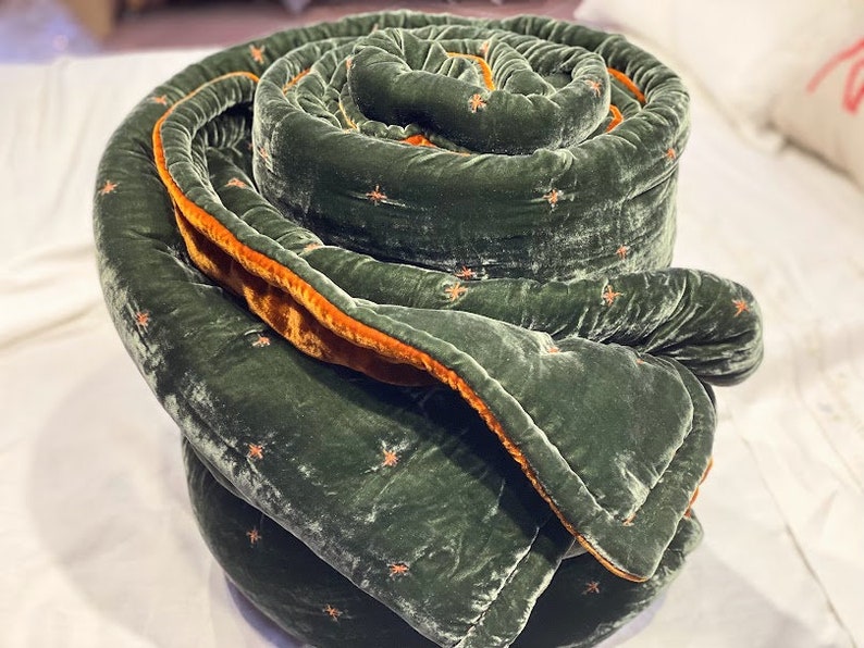 May include: A green velvet quilted throw blanket with a brown velvet trim. The blanket is rolled up in a spiral shape.