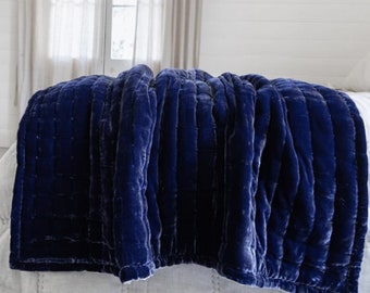 May include: A navy blue velvet quilted throw blanket with a soft, plush texture. The blanket is folded and draped over a bed, showcasing its luxurious feel.