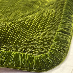 May include: A green velvet quilted throw blanket with a ruffled edge. The blanket is made of a soft, luxurious fabric and has a subtle sheen.