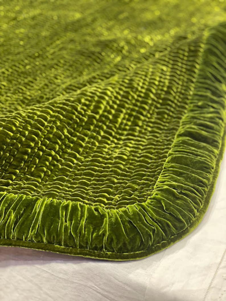 May include: A green velvet quilted throw blanket with a ruffled edge. The blanket is made of a soft, luxurious fabric and has a subtle sheen.