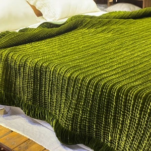 May include: A green velvet quilted throw blanket with a ruffled edge. The blanket is folded and displayed on a bed.