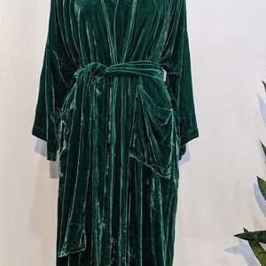 May include: A long, dark green velvet robe with a shawl collar and a tie belt. The robe has two large pockets on the front.