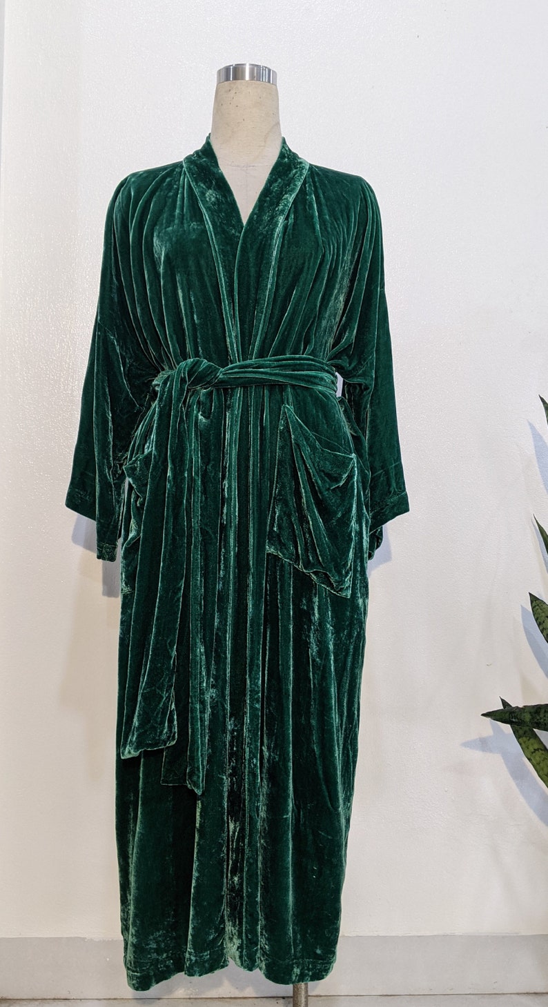 May include: A long, dark green velvet robe with a shawl collar and a tie belt. The robe has two large pockets on the front.