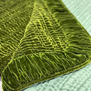 May include: A green velvet quilted throw blanket with a ruffled edge. The blanket is folded in half and the underside is a light blue color.