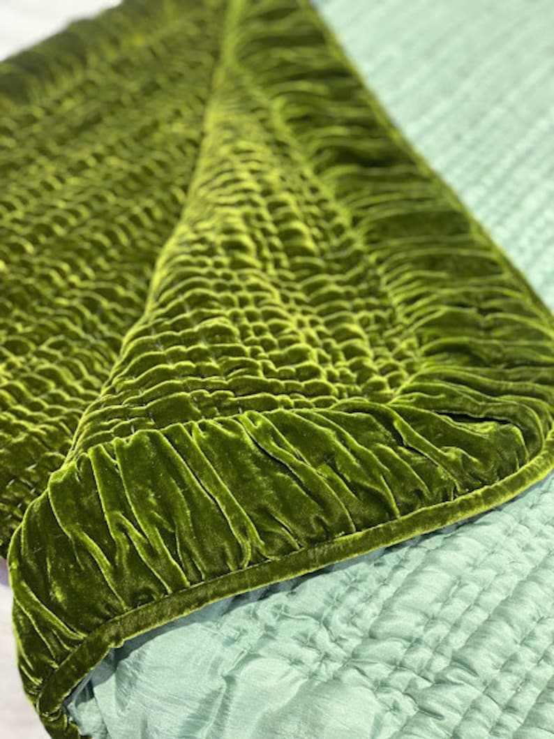 May include: A green velvet quilted throw blanket with a ruffled edge. The blanket is folded in half and the underside is a light blue color.