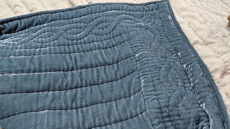 May include: A blue velvet quilted throw blanket with a decorative pattern. The blanket is soft and luxurious, perfect for adding a touch of elegance to any room.