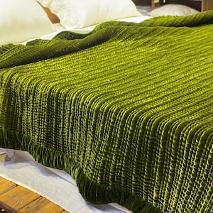 May include: A green velvet quilted throw blanket with a ruffled edge. The blanket is folded and displayed on a bed.