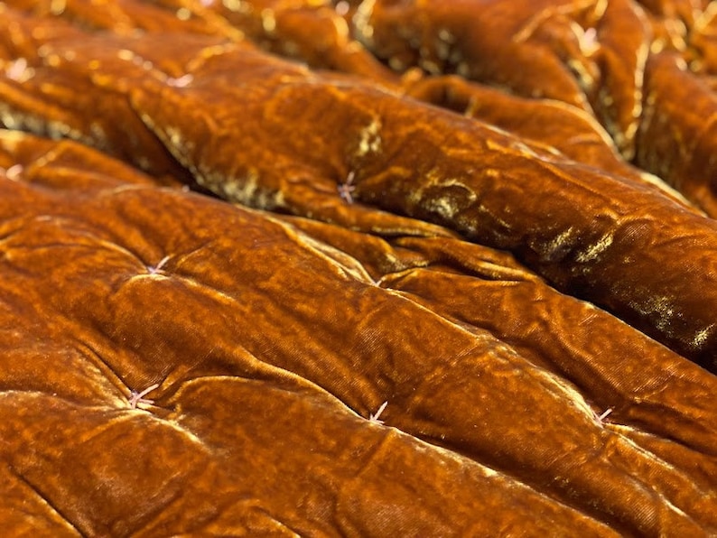 May include: Close-up of a brown velvet quilted blanket with a subtle sheen. The blanket is folded and the stitching is visible.