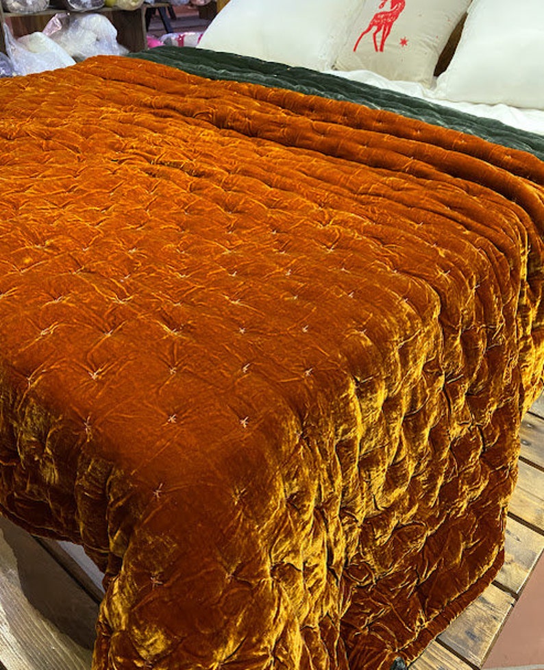 May include: A quilted velvet throw blanket in a rich orange color. The blanket has a subtle diamond pattern and is made of a soft, luxurious fabric.