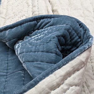 May include: A blue velvet quilt with a white linen backing. The quilt is folded in half, showing the stitching detail on the linen side.
