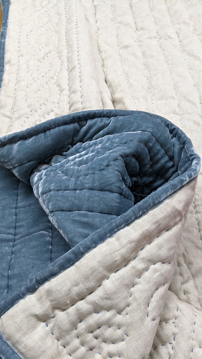 May include: A blue velvet quilt with a white linen backing. The quilt is folded in half, showing the stitching detail on the linen side.