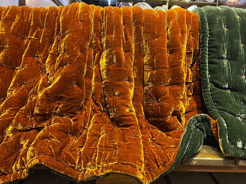 May include: A quilted throw blanket with a deep orange velvet side and a dark green velvet side. The blanket is folded in half, showing both sides.