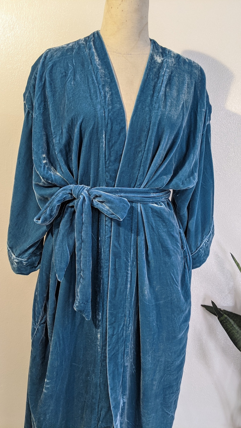 May include: A teal blue velvet robe with a self-tie sash. The robe has a V-neck and long sleeves.