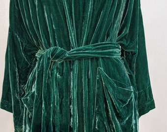 May include: A long, dark green velvet robe with a shawl collar and a tie belt. The robe has two patch pockets on the front.