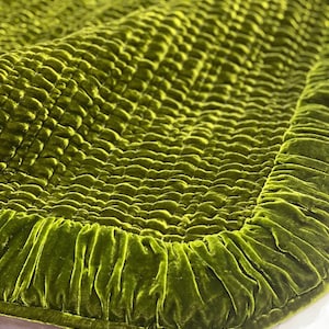 May include: A green velvet quilted throw blanket with a ruffled edge.