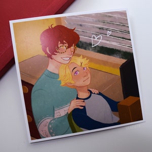 May include: A digital illustration of two men, one with red hair and glasses, the other with blonde hair, hugging each other. The man with red hair is wearing a light blue sweater with a white pattern. The man with blonde hair is wearing a blue and gray shirt. The background is a yellow and brown room with a computer screen and a brown box.