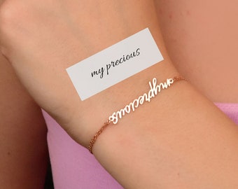 May include: A gold chain bracelet with the word "grandmother" written in cursive on it. A white note with the text "my precious" is visible in the image.