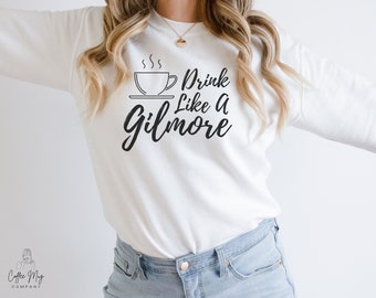 Könnte beinhalten: Weißer Pullover mit einer schwarzen Grafik einer Kaffeetasse und dem Text "Drink Like A Gilmore".
