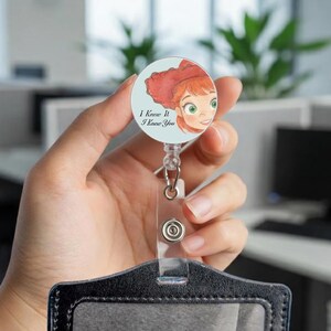 May include: A circular badge reel featuring a watercolor illustration of a red-haired character with green eyes on a light blue background. The text "I Knew It I Knew You" is printed in black. The reel has a clear plastic strap with a metal snap button.