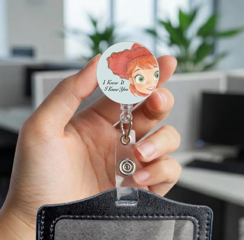 May include: A circular badge reel featuring a watercolor illustration of a red-haired character with green eyes on a light blue background. The text "I Knew It I Knew You" is printed in black. The reel has a clear plastic strap with a metal snap button.