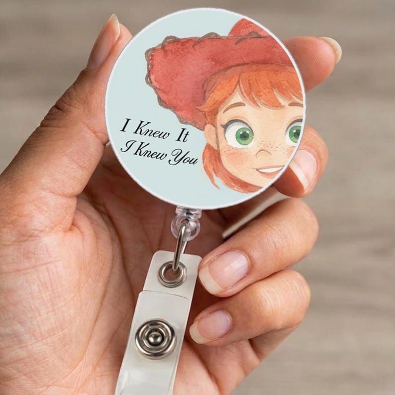 May include: A circular badge reel featuring a light blue background and a watercolor illustration of a person with red hair wearing a red cowboy hat. The text "I Knew It I Knew You" is printed in black script on the left side of the badge reel.